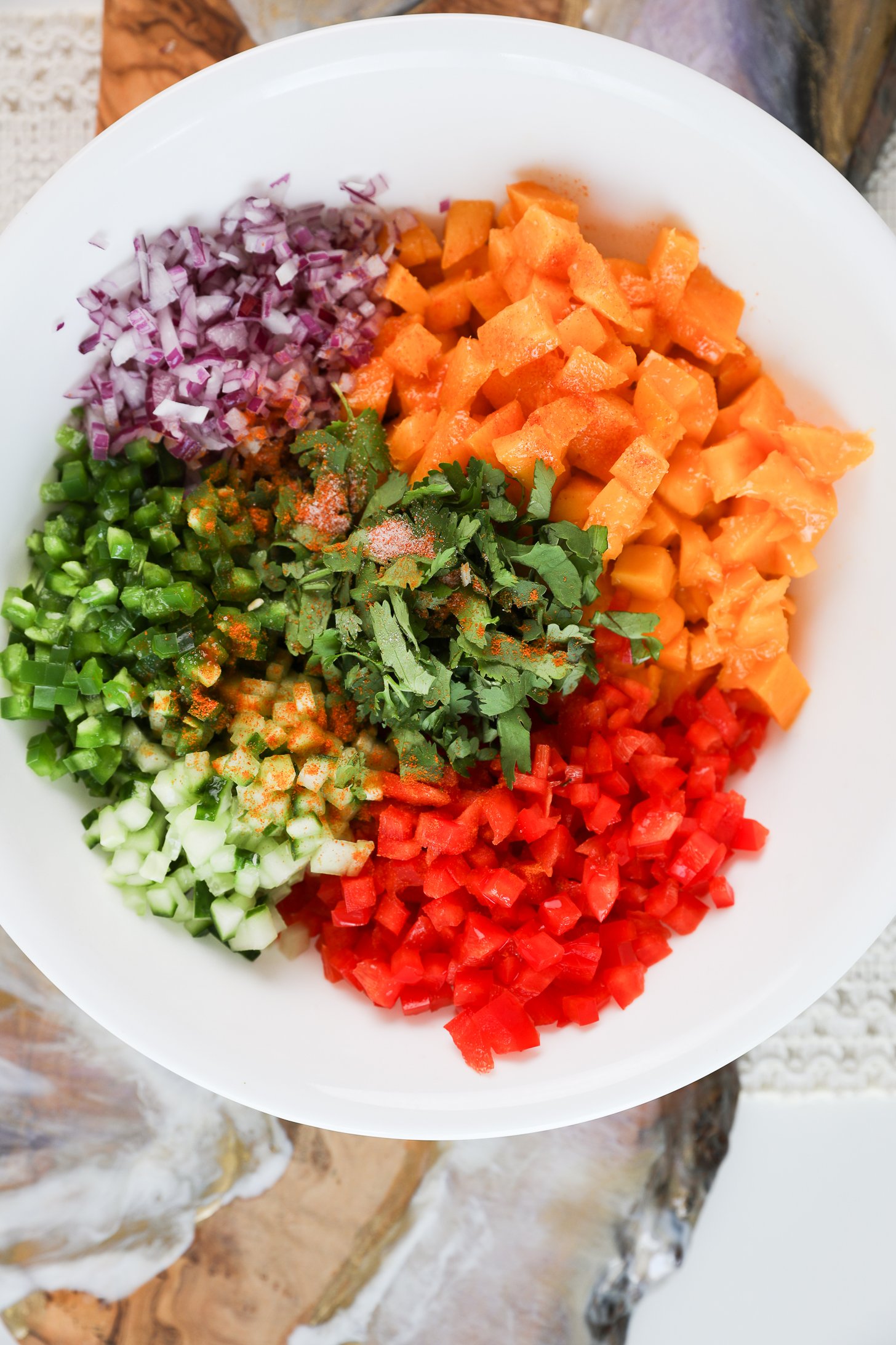 A bowl of diced produce including mangoes, pepper, onion, cucumber, cilantro and jalapeno, topped with salt and spice.