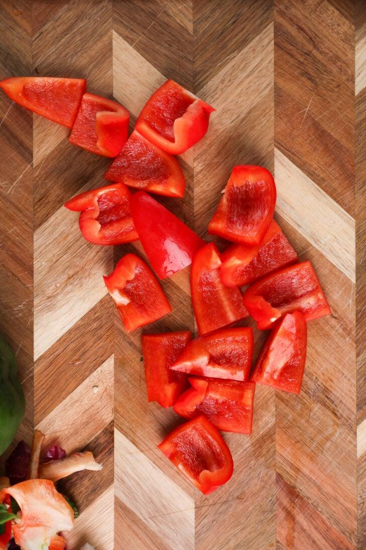 Red bell pepper chunks on a wooden board.