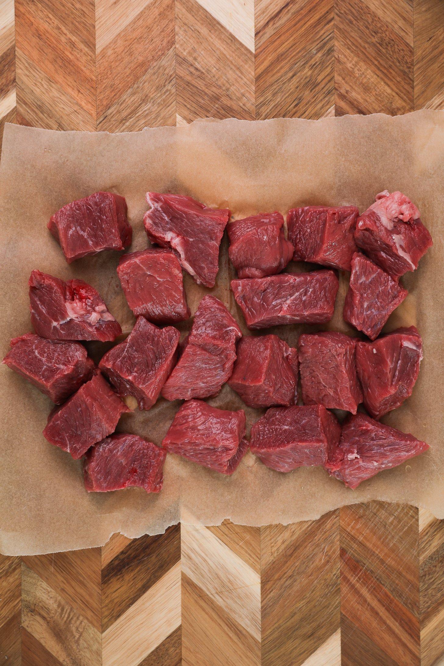 Cubes of sirloin beef on parchment paper placed on a wooden board.