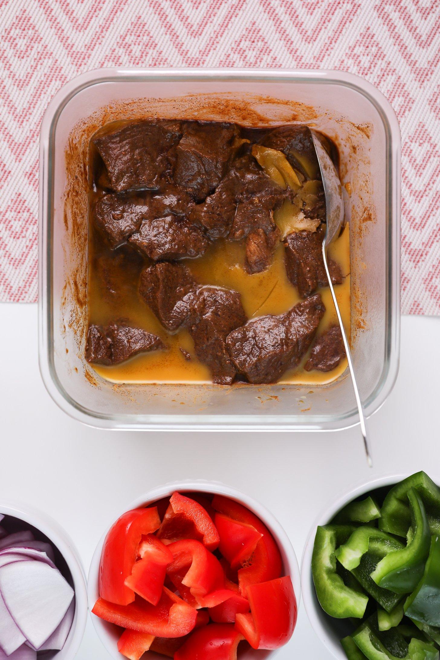 A glass container of beef cubes submerged in a marinade that is solidified because of the fat.