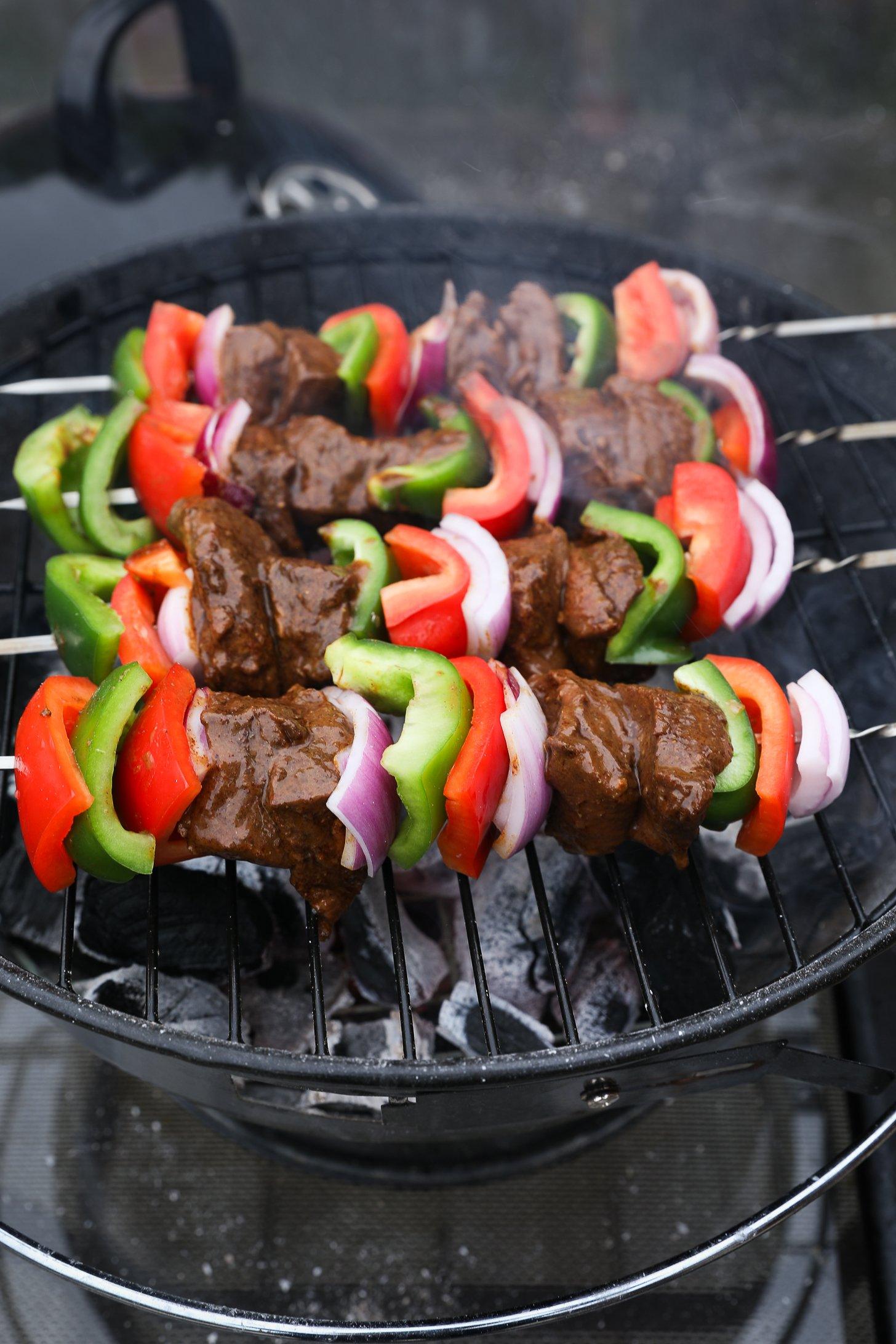 Marinated beef and veggie skewers grilling on a charcoal grill.