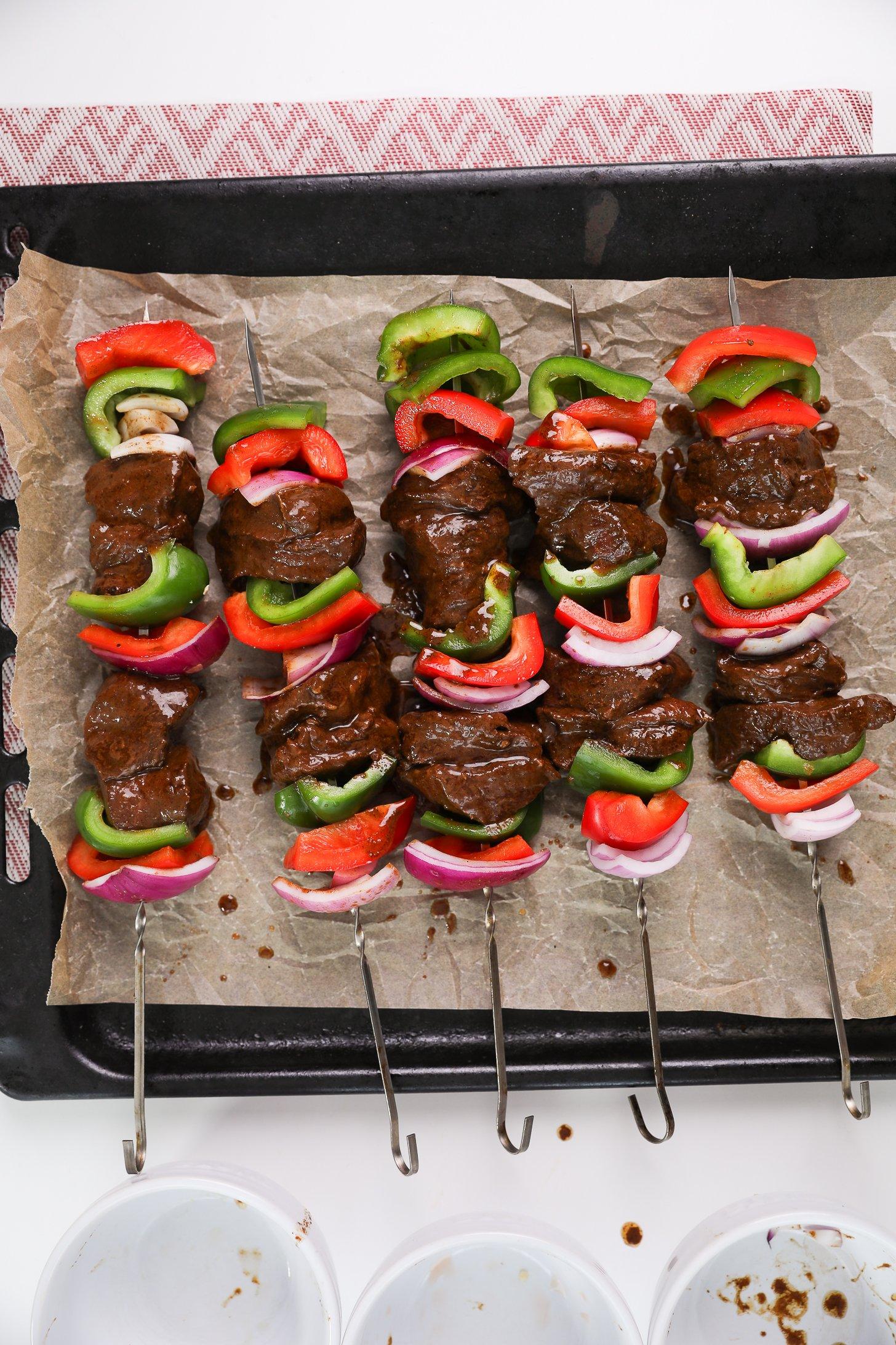 A tray with skewers of raw marinated beef cubes and peppers, ready for grilling.