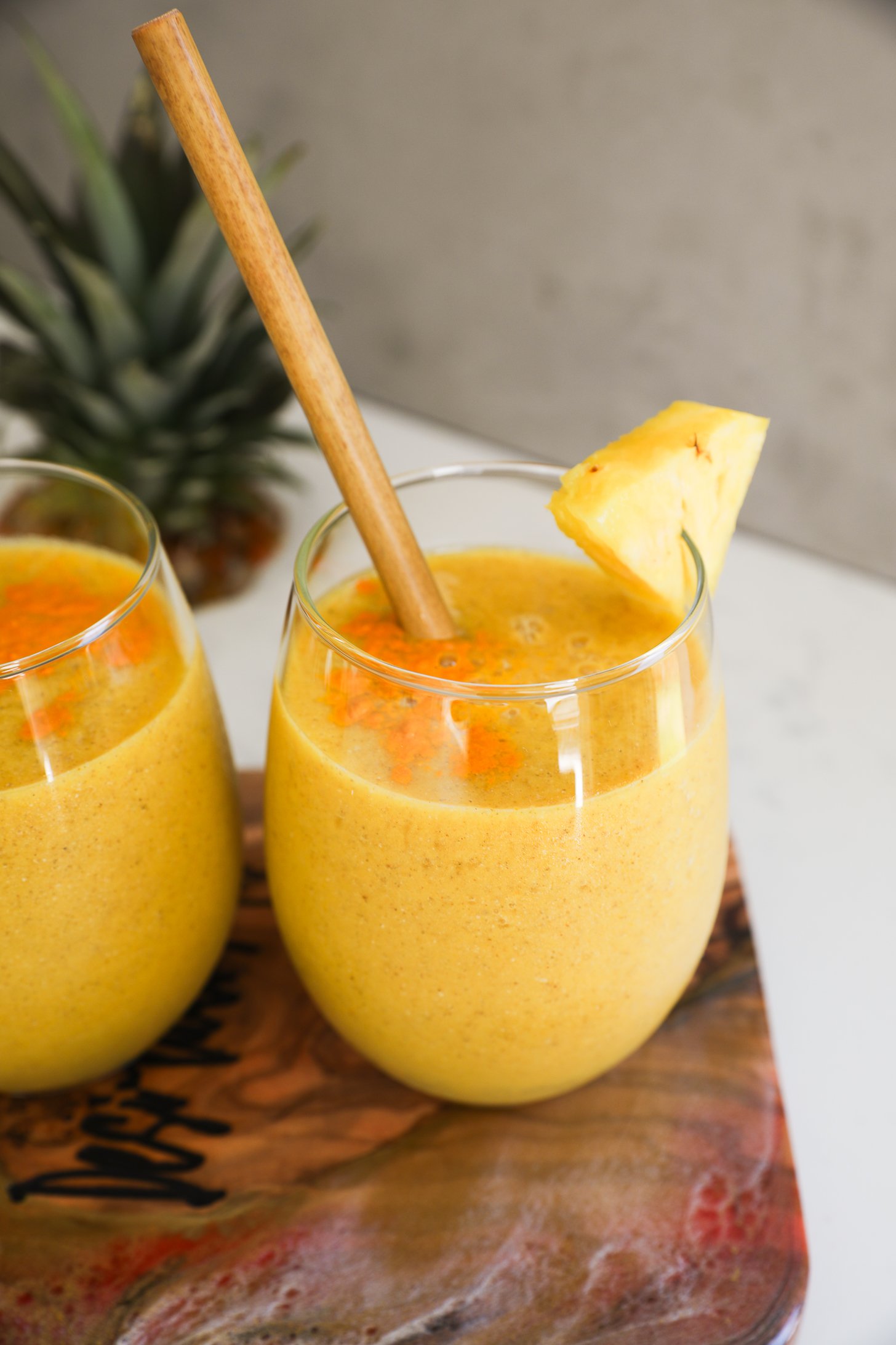 Perspective image of glasses of yellow smoothie topped with turmeric powder.