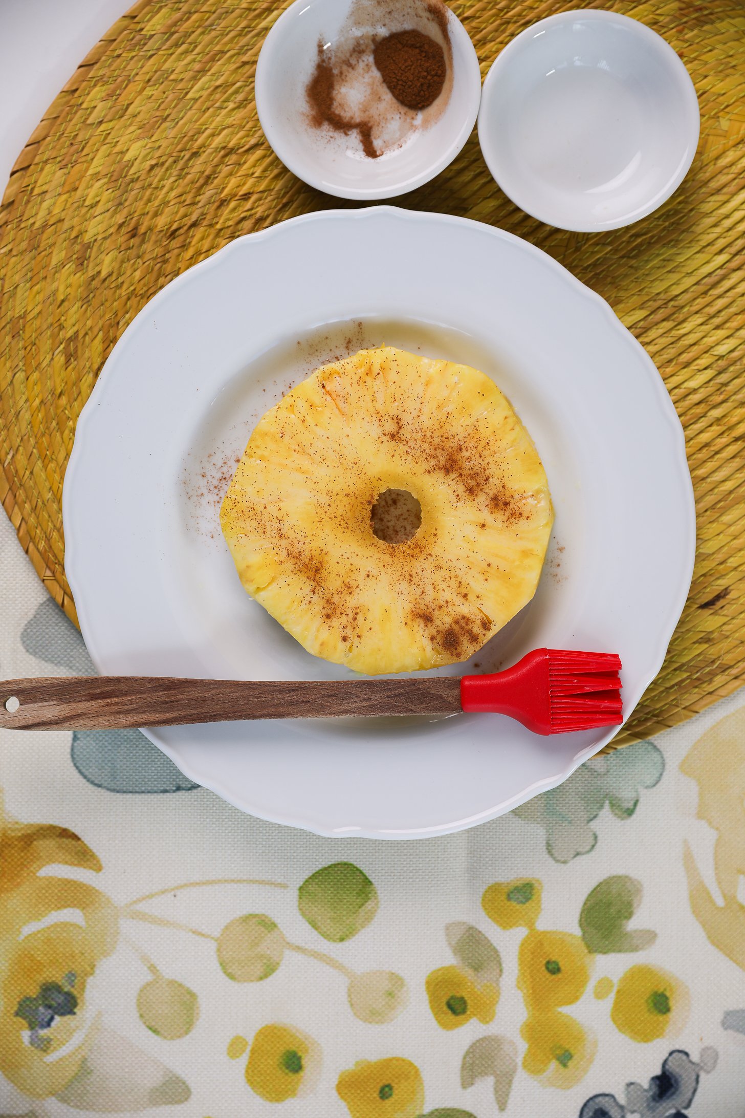 A ring of fresh pineapple sprinkled with cinnamon powder on a plate with a brush next to it.