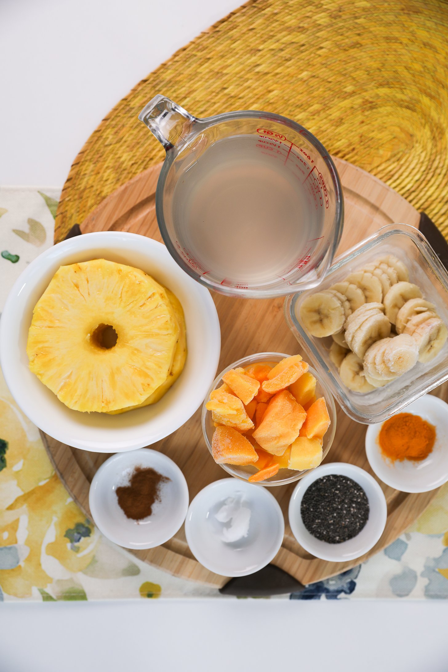 A selection of food ingredients including pineapple rings, mango chunks, banana slices, chia seeds, spices and coconut water.