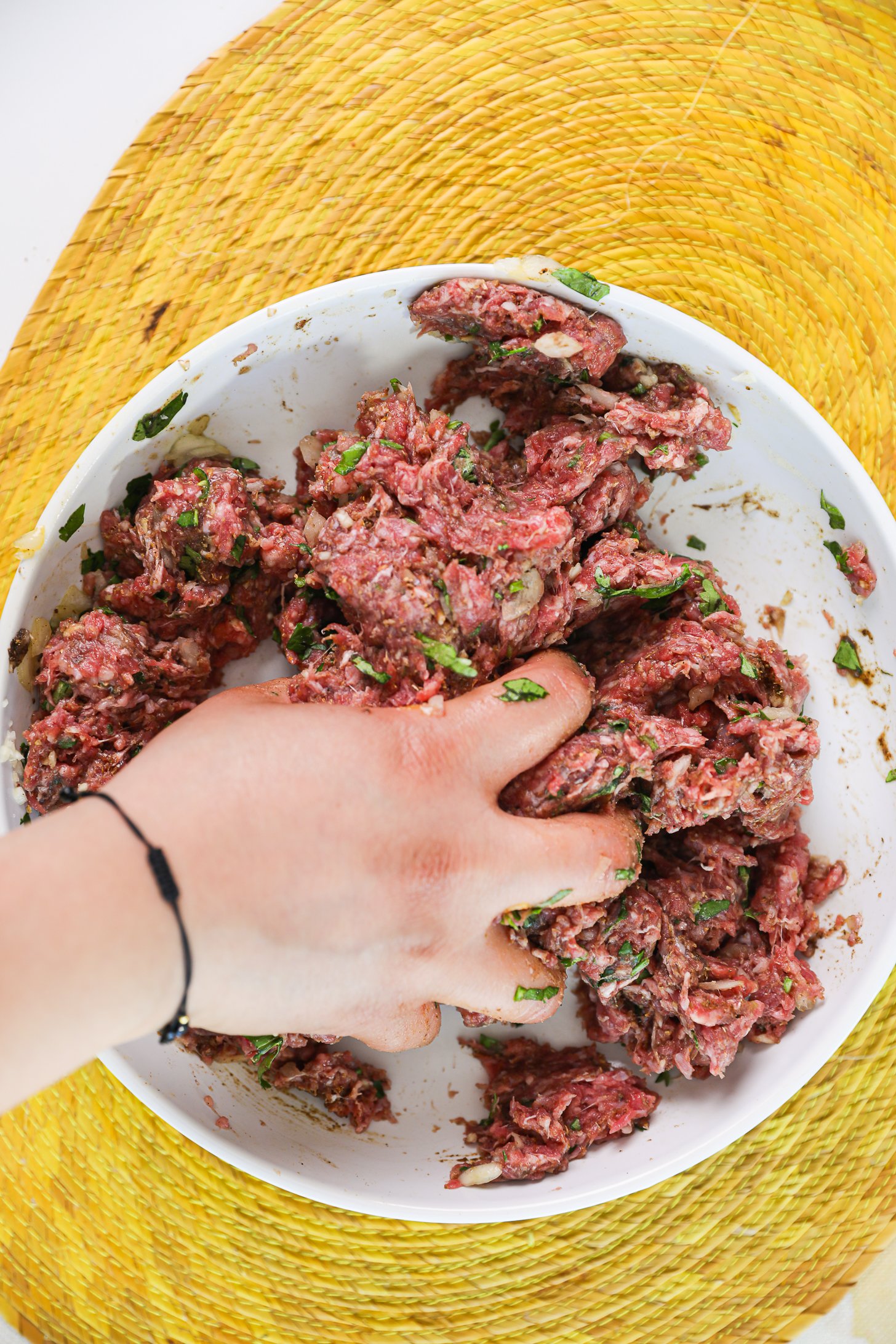 A hand squashing raw minced beef in a bowl.