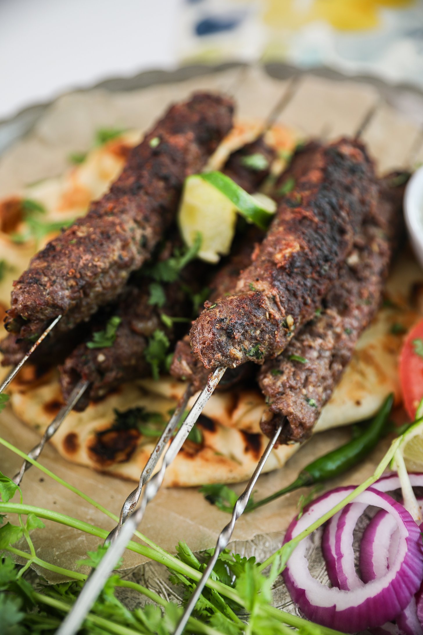 Perspective view of grilled beef kebabs on skewers atop a naan.