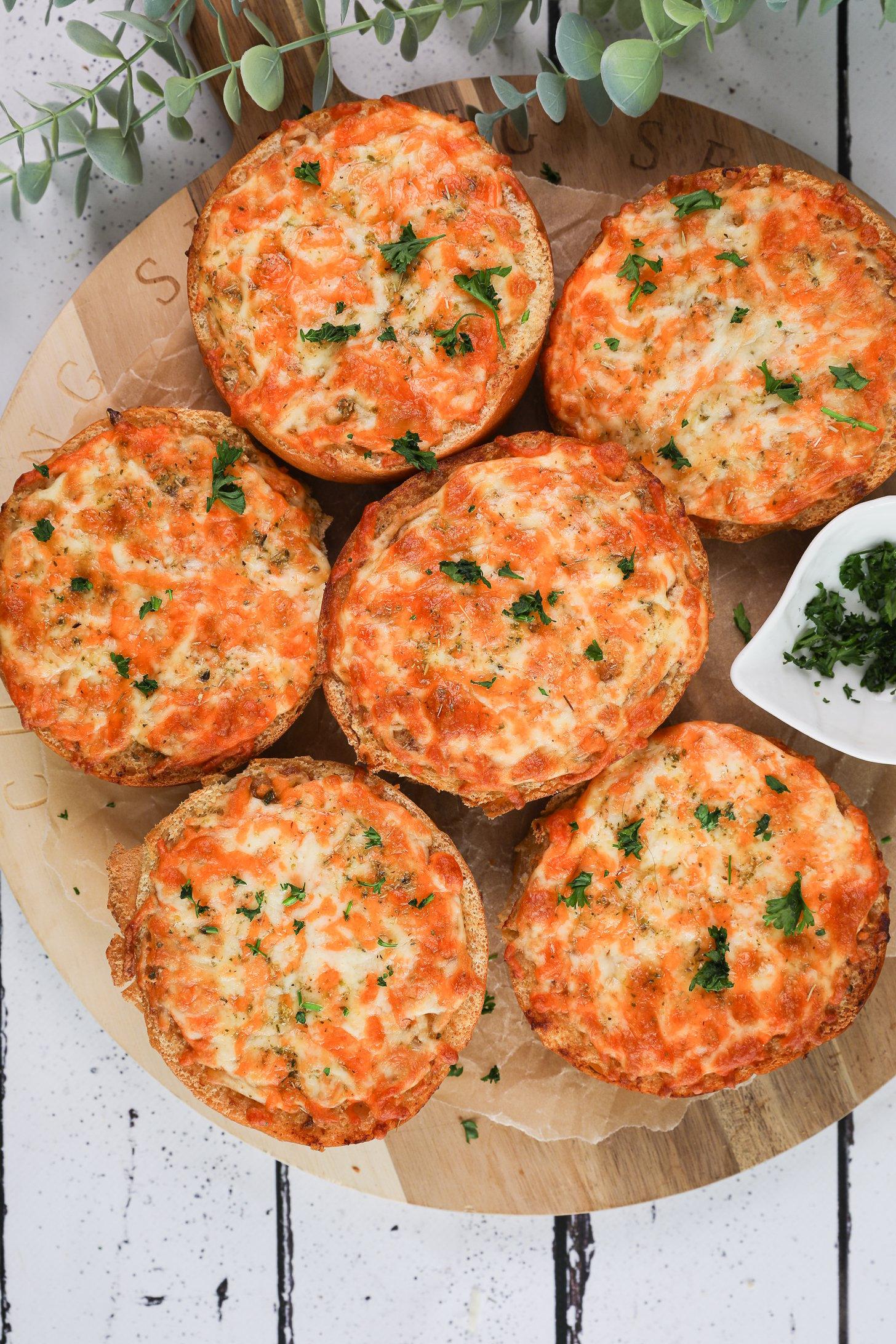 Overhead image of six round cheesy garlic breads on a wooden board.