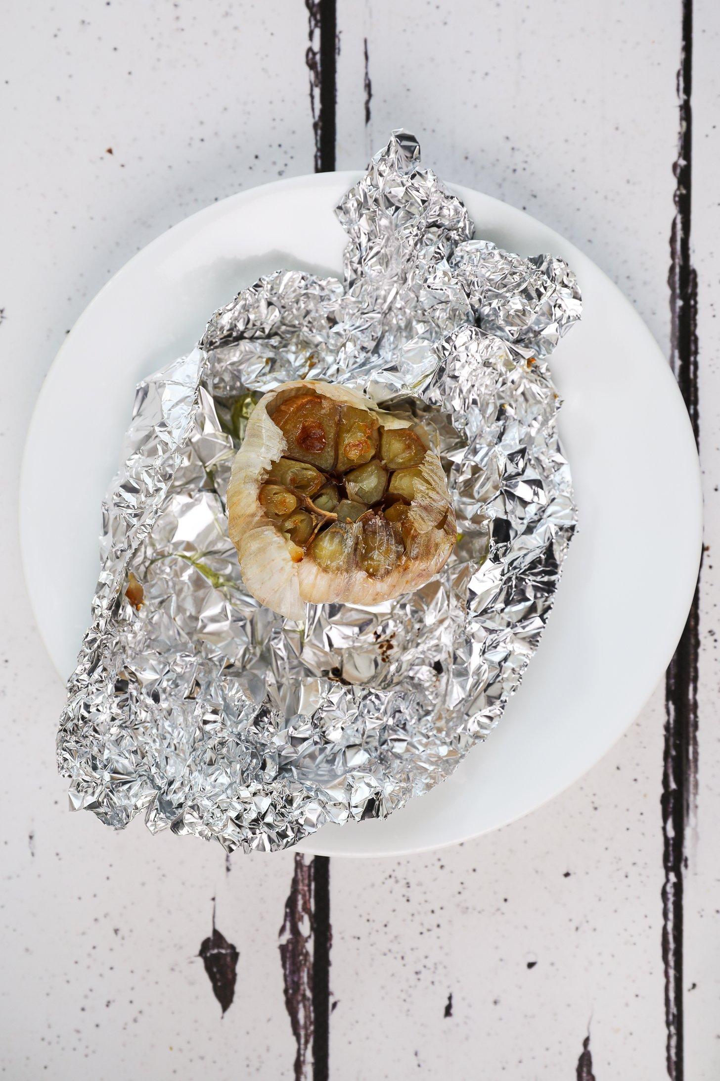 A roasted garlic bulb on crinkled foil on a plate.