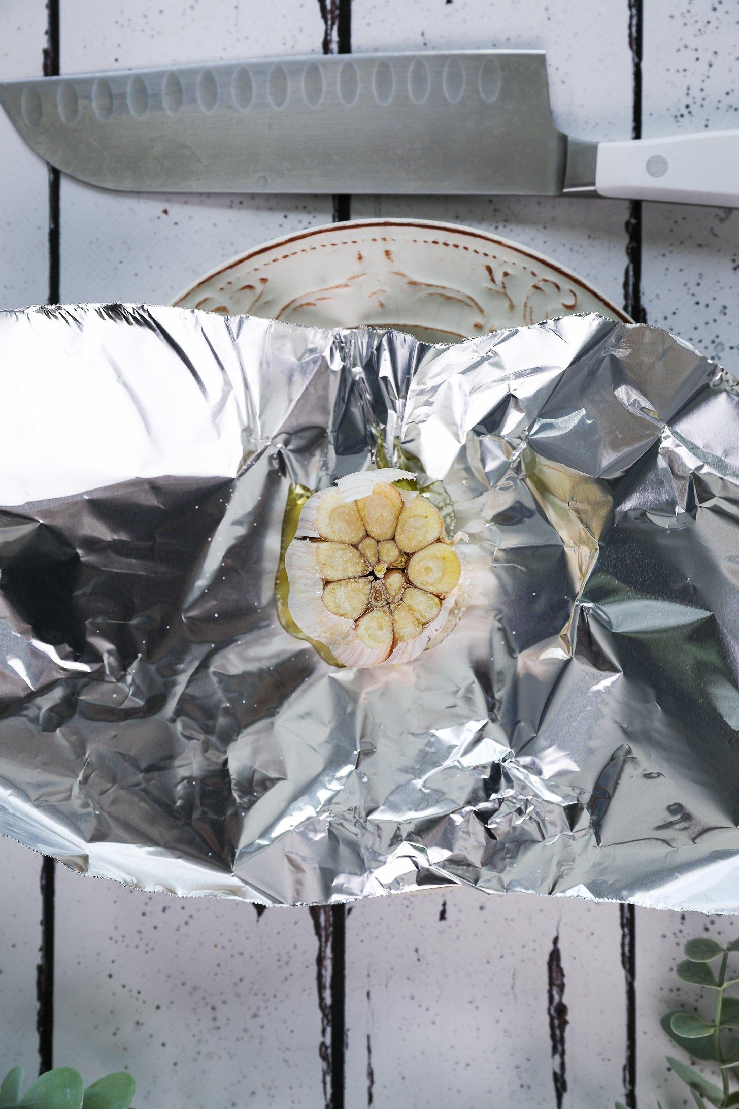 An oil-coated garlic bulb placed on foil with a knife close by.