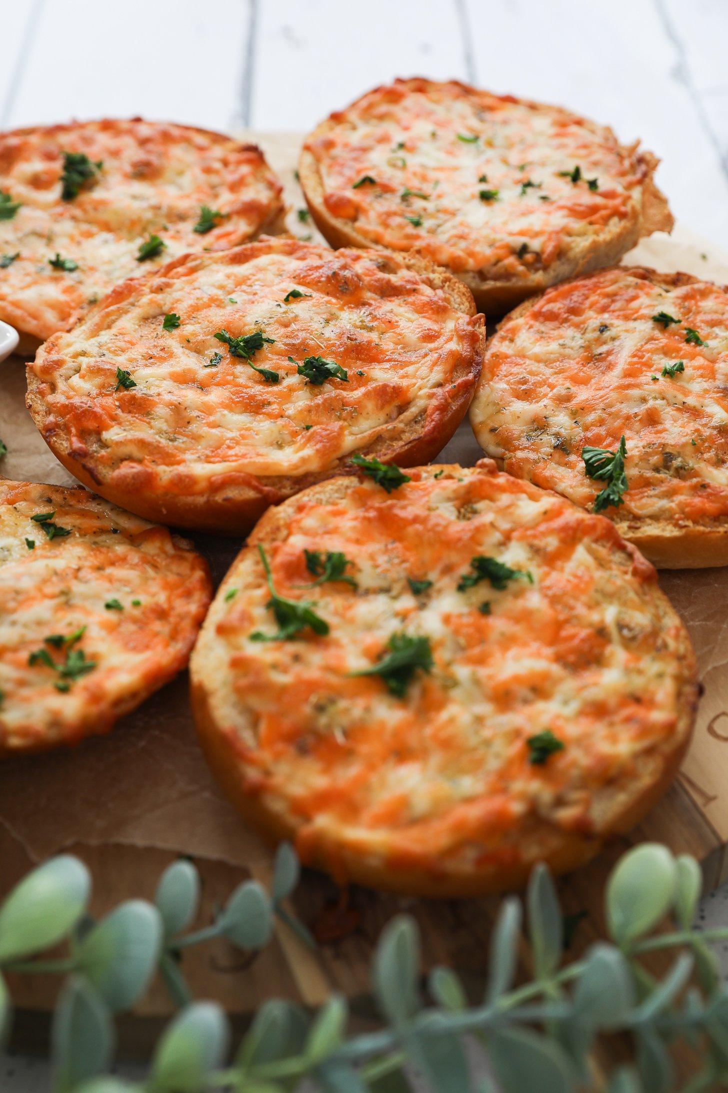 Perspective image of round cheesy garlic breads with a plant in the foreground.