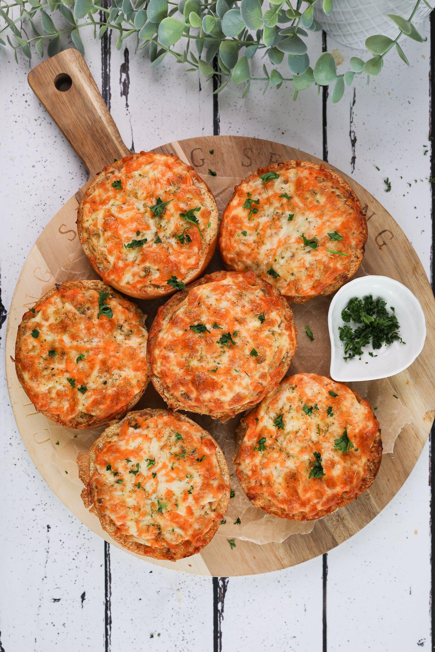 Birdseye image of of six round cheesy garlic breads on a wooden board with a plant nearby.