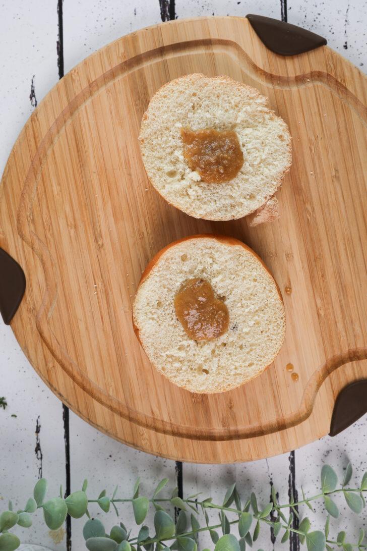 Two halves of a round Kaiser roll topped with a spoonful of roasted garlic butter.