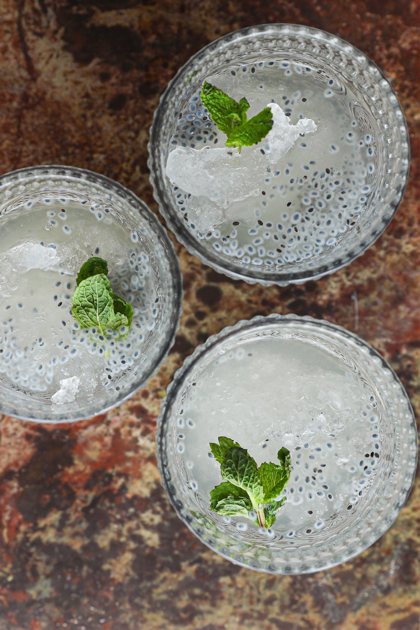 A close-up image of 3 glasses filled with ice, water and basil seeds with sprigs of mint in each.
