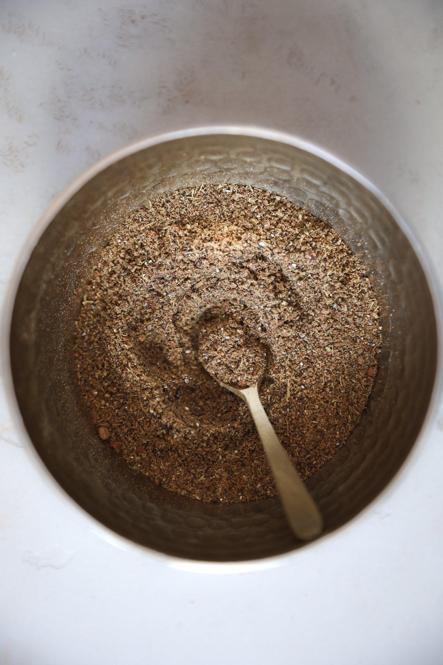 Top view of a spoon resting in a bowl of chai masala spice blend.