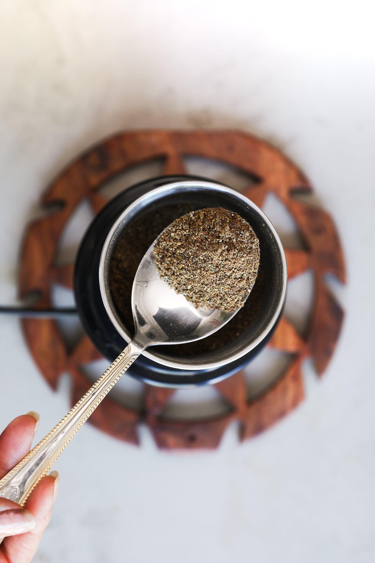 A spoonful of chai masala hovers over a spice grinder after blending.