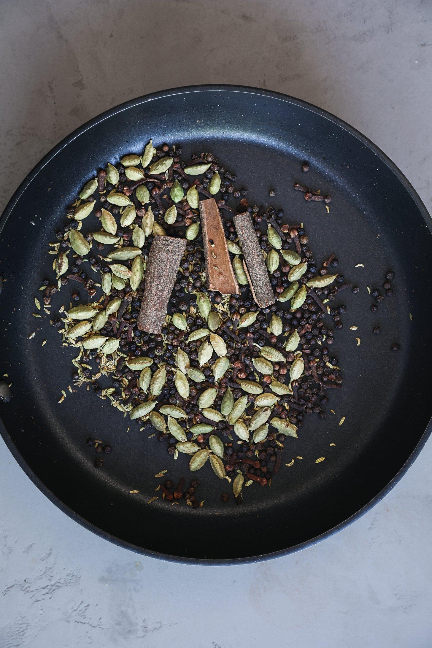 Cardamom, cinnamon, and spices gently toasting in a pan for chai masala.