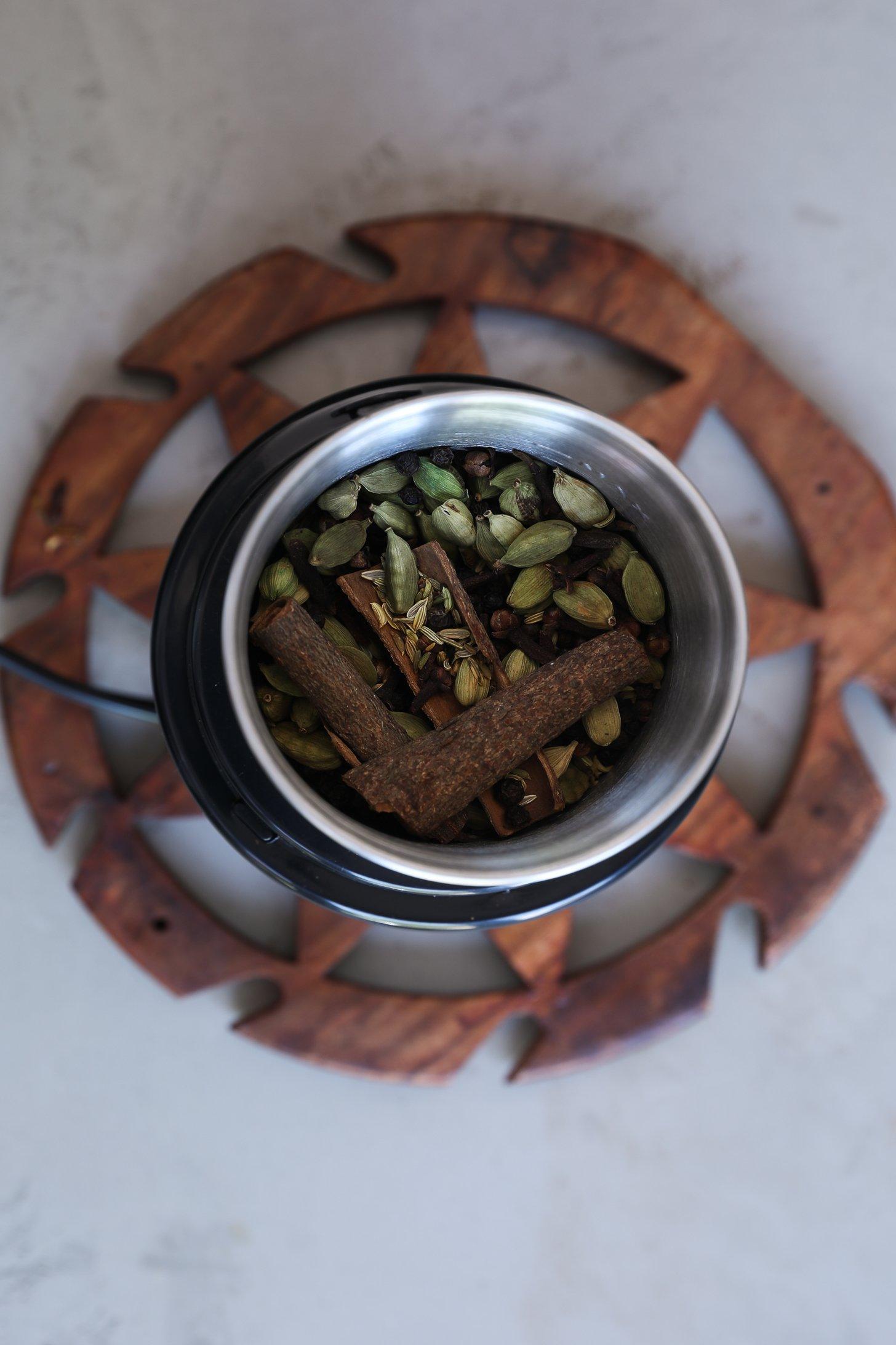 Whole chai masala spices in a grinder, ready to be pulsed into a blend.