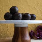 Group of chocolate coconut ladoos on a white marble pedestal with a wooden base, styled against a golden textured wall.