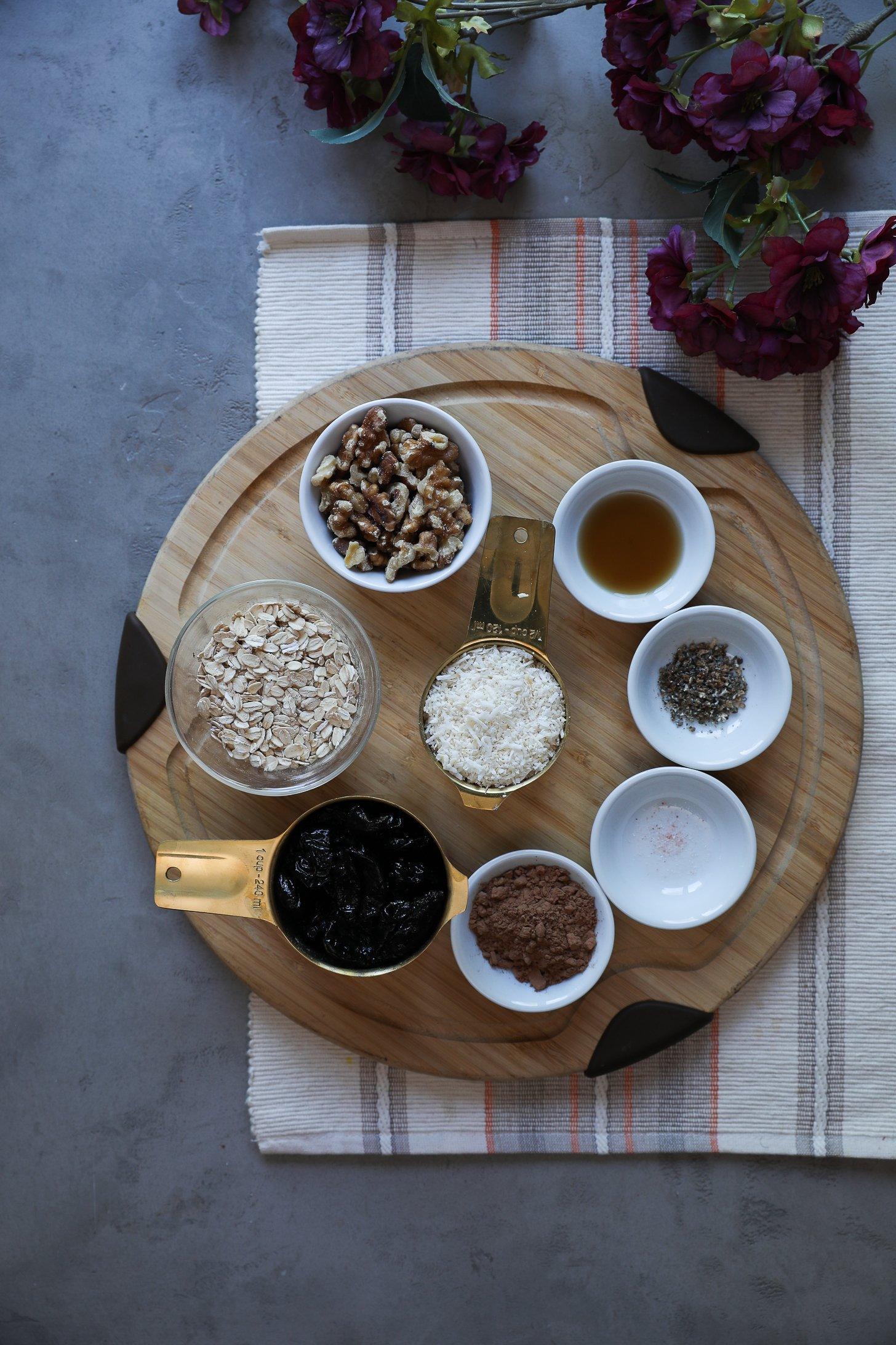 Overhead view of measured ingredients for no-cook chocolate coconut ladoos, including prunes, oats, shredded coconut, walnuts, cocoa powder, and spices.