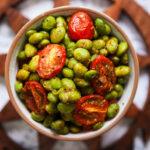Close-up of roasted edamame and cherry tomato Indian chaat in a ceramic bowl.