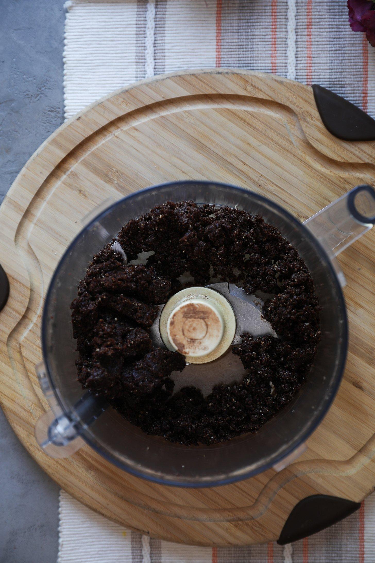 Chocolate coconut ladoo mixture blended in a food processor, dark and sticky with visible texture.