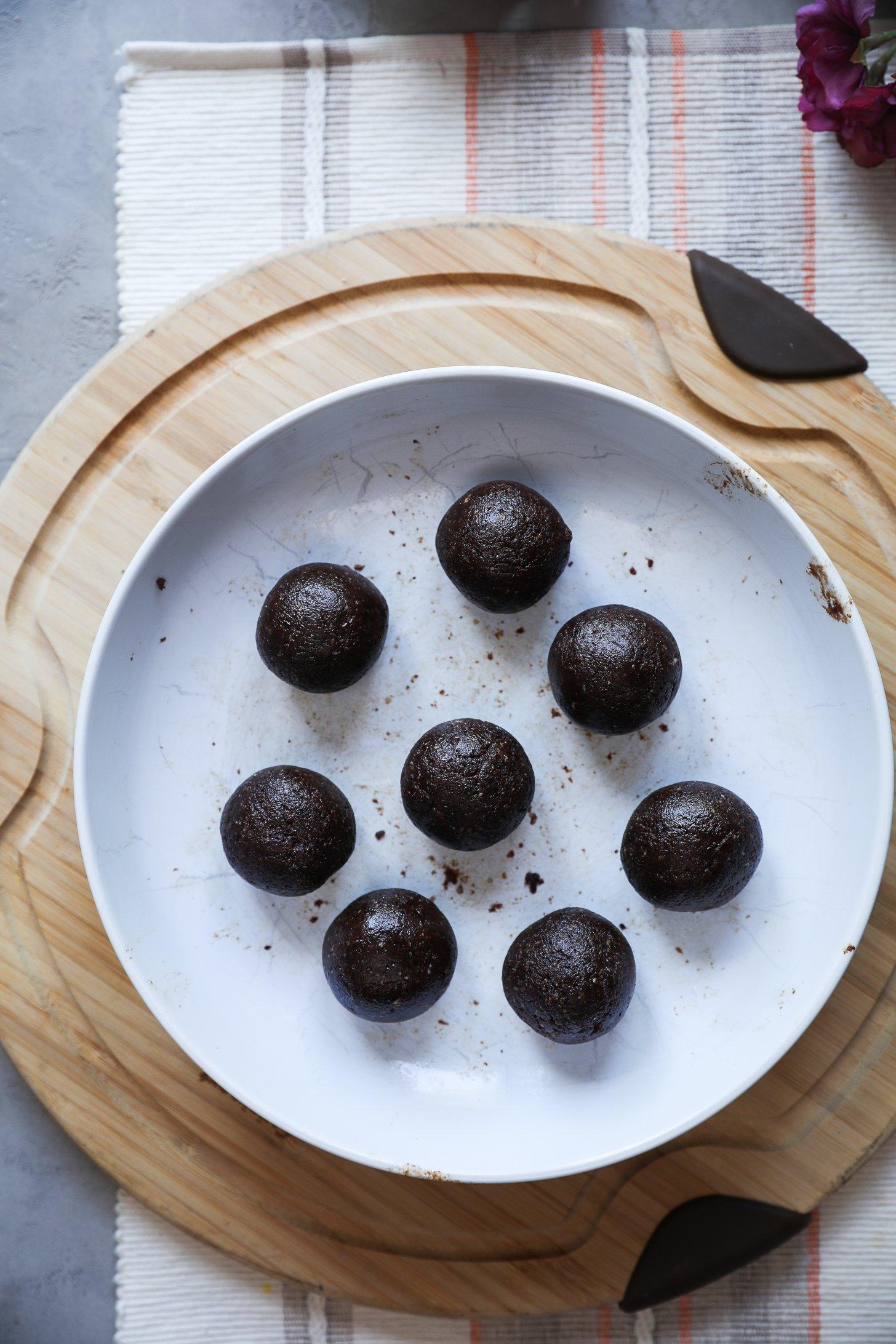 Eight perfectly rolled chocolate coconut ladoos arranged on a white plate, ready to chill.