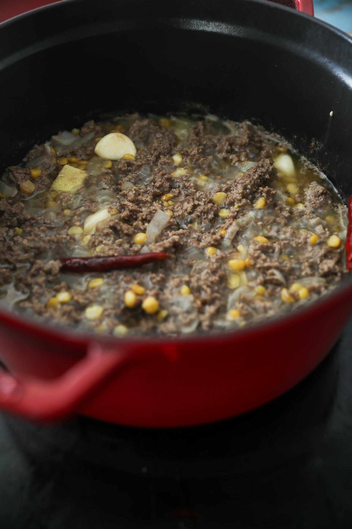 Minced beef, chana dal, and spices simmering in a red Dutch oven.