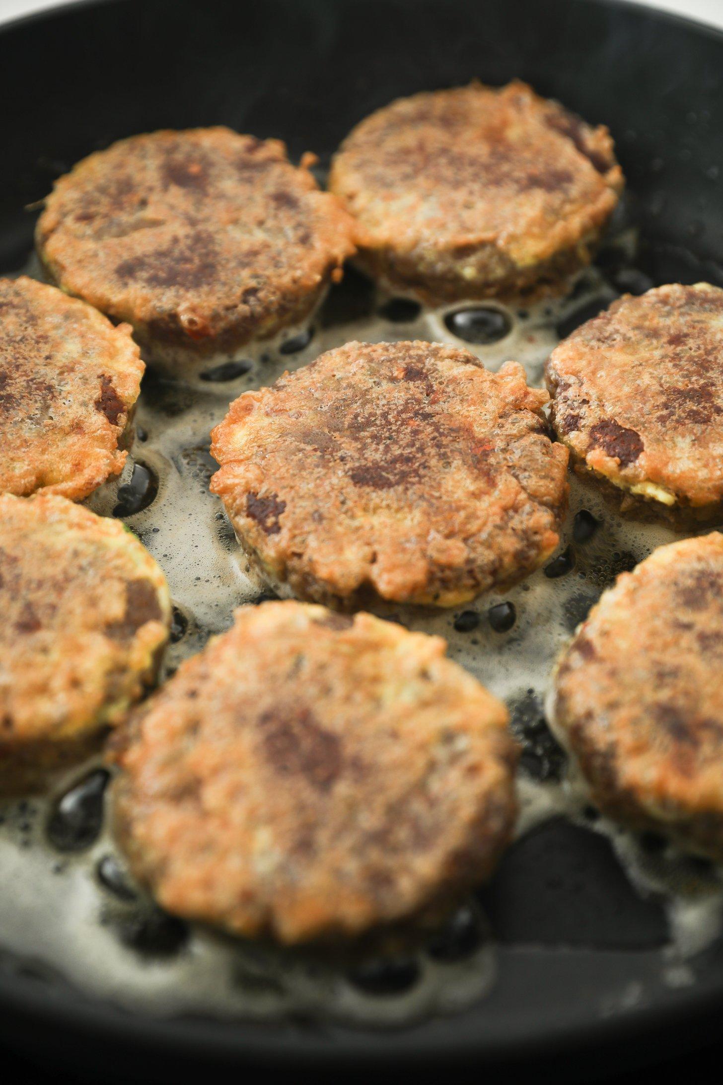 Beef kebabs sizzling in oil in a skillet.