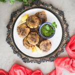 Overhead view of golden beef kebabs with chutney and lemon slices.