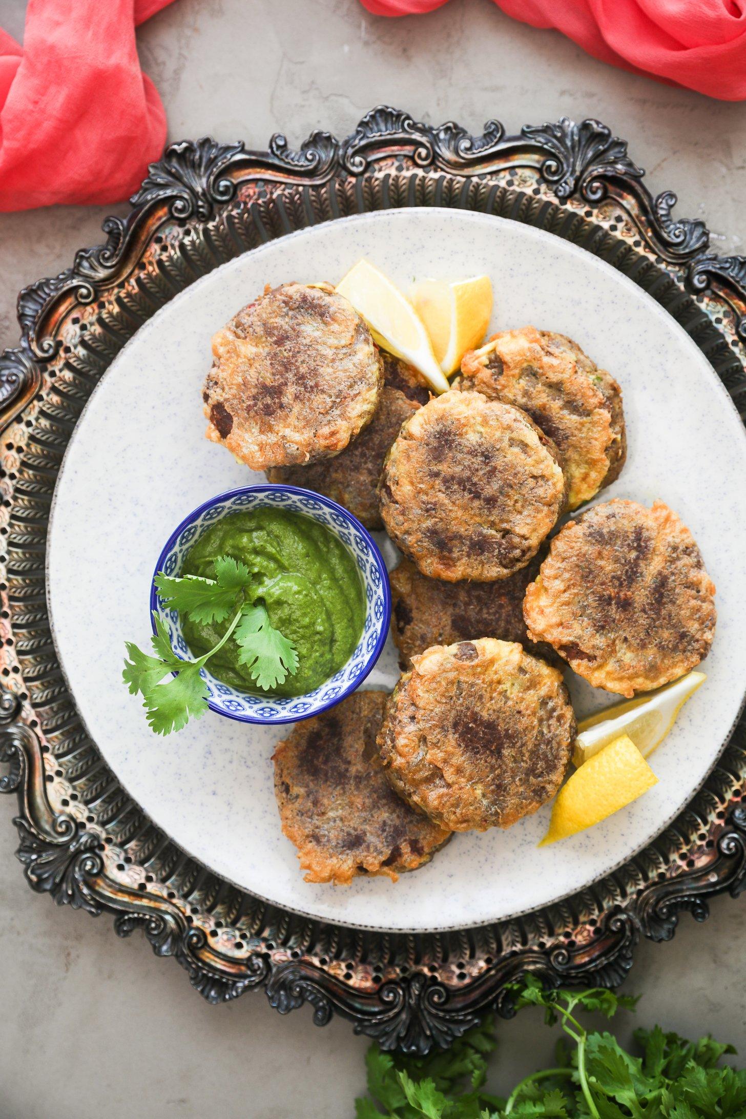 Plate of stovetop shami kebabs served with green chutney and lemon wedges.