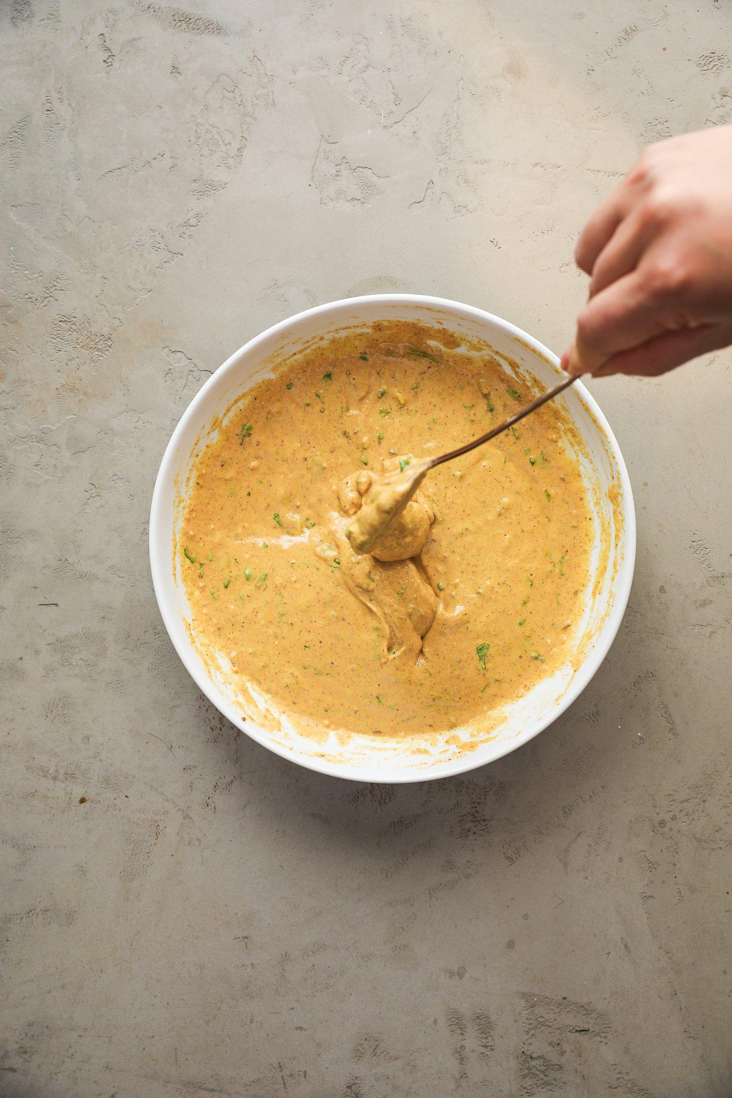 Hand holding a spoon dipped in spiced chickpea batter.