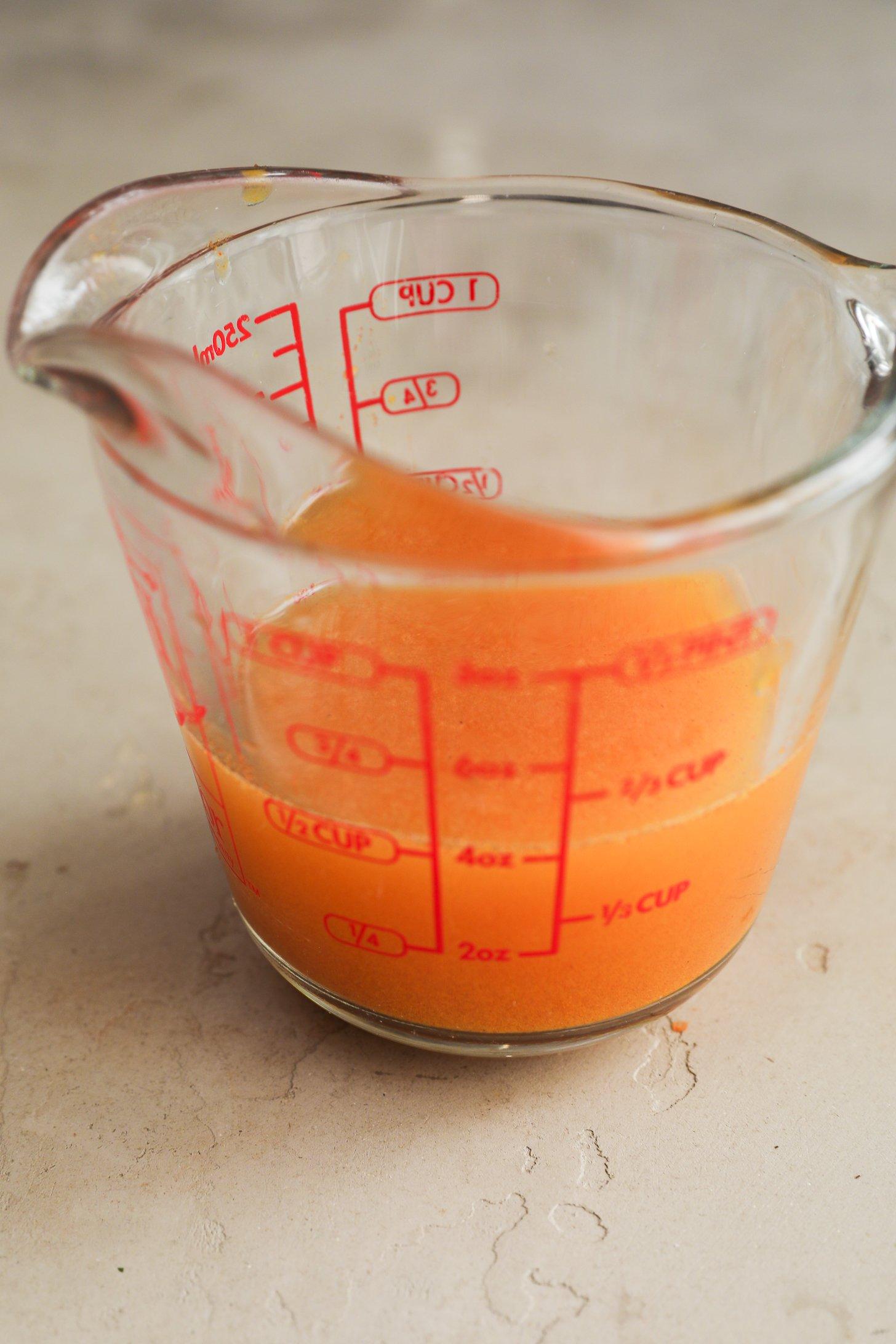 Clear glass measuring jug showing leftover orange liquid.