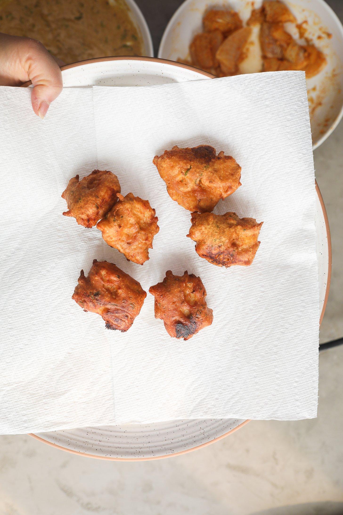 Golden crispy basa fish pakora fritters resting on a white paper towel-lined plate.