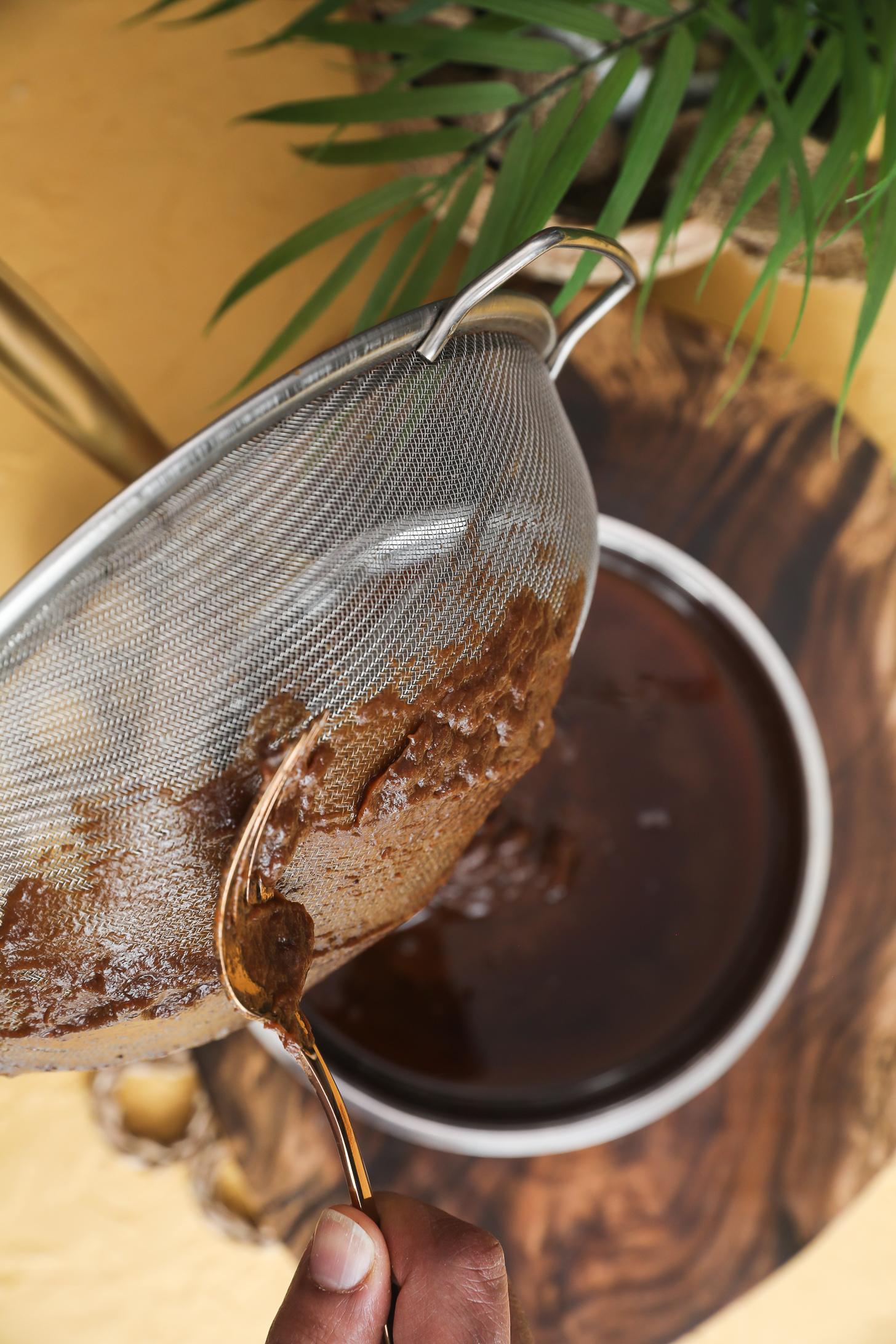 Spoon scraping tamarind pulp from back of sieve into pan.