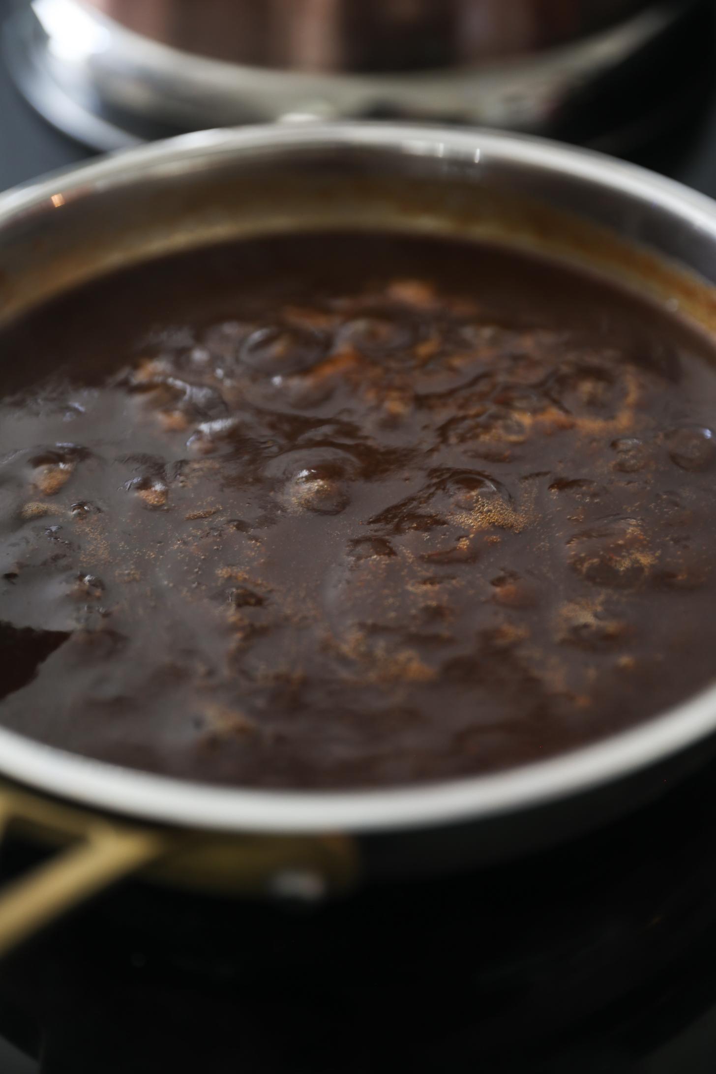 Tamarind chutney simmering in saucepan with bubbles forming.