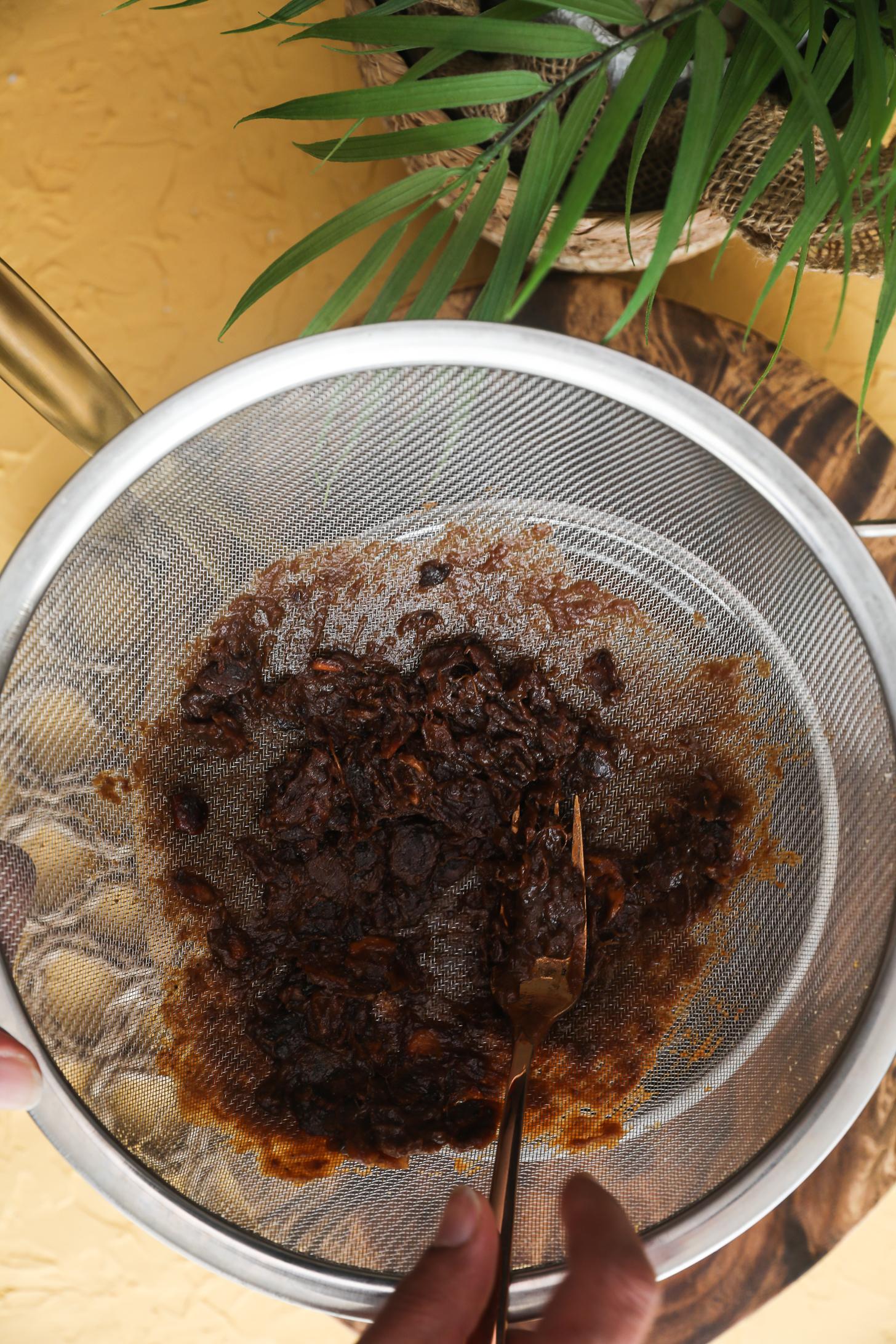 Tamarind pulp being pressed through sieve with fork.